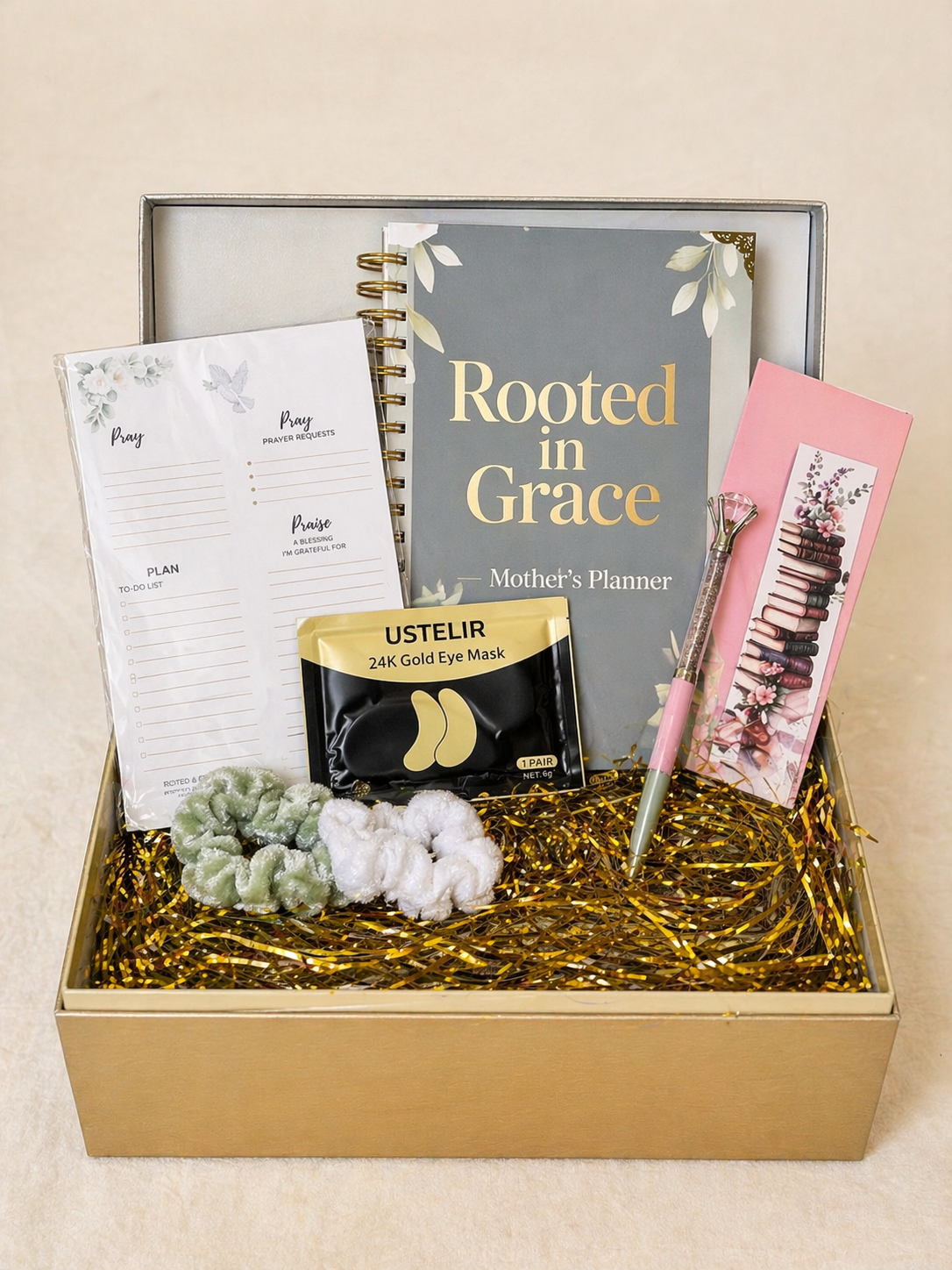 Gift box with 'Rooted in Grace' planner, gold eye mask, pen, and stationery items on a beige background