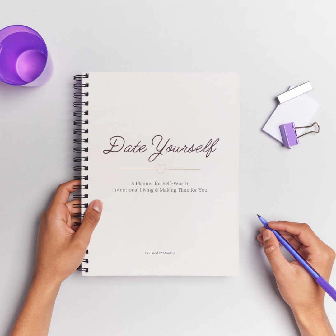 Notebook titled 'Date Yourself' with hands holding a pen on a light gray background