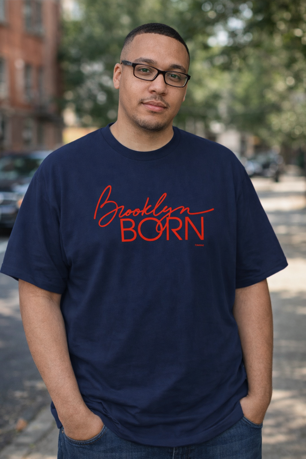 Man wearing a navy blue t-shirt with 'Brooklyn Born' in red text, standing outdoors.
